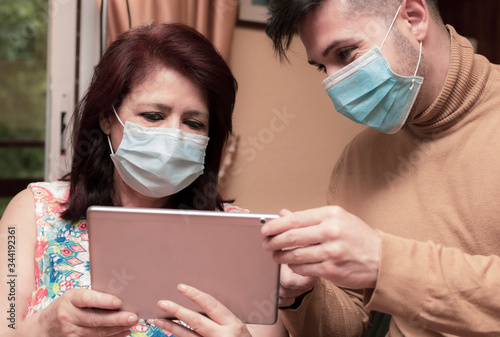 son helps his mother to use tablet. older people using technology Wear pandemic face masks. covid-19