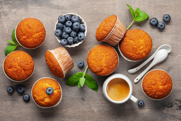 Wall Mural - Muffins or capcakes with blueberries and mint, a cup of coffee on a wooden background. Top view