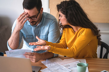 Wall Mural - Young unhappy couple arguing about money bills and expenses at home stock photo