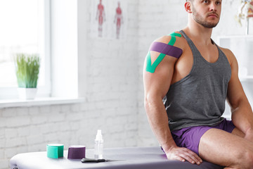 Wall Mural - Kinesiology taping. Kinesiology tape on patient shoulder. Injured shoulder treatment of young male athlete. Post traumatic rehabilitation, sport physical therapy, recovery concept.