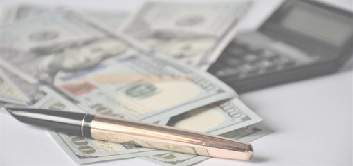 blurred light background, a pile of dollars banknotes on a white background, with a golden pen and calculator, business concept