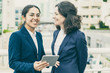 © Mangostar - Happy businesswomen with digital tablet. Cheerful professional female colleagues standing with digital tablet on urban city street. Wireless technology concept