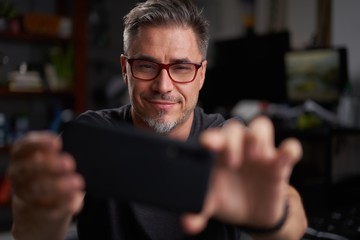 man using smart phone at home sitting in armchair in cosy living room.