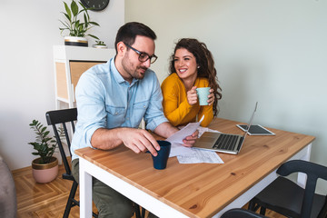 Wall Mural - Smiling couple managing finances, reviewing their bank accounts using laptop computer and calculator at modern kitchen stock photo