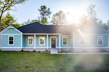 Front view of a brand new construction house with blue siding, a ranch style home with a yard and a sun lens flare