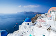 Panorama from Oia, blue domes of orthodox church and the caldera with boats in the back, Santorini island, Greece