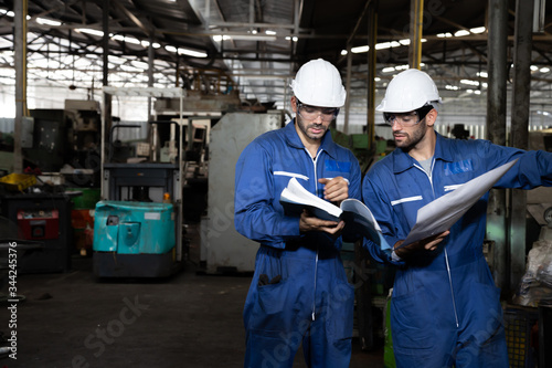 Fotografía Factory engineer reading manual of machine operation and standing with blue working suite dress and safety helmet