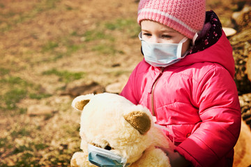  Small child in a medical mask close-up. A child with a soft toy waits for the end of quarantine. The kid is waiting for the end of quarantine and the pandemic of coronavirus infection
