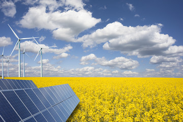 Renewable or green energy concept with wind turbines solar panels and yellow raps field on blue sky with clouds