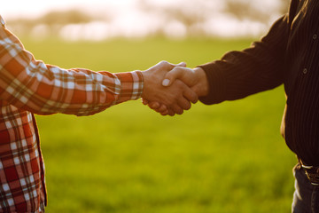 Handshake two farmer on the background of a wheat field at sunset. The concept of the agricultural business.