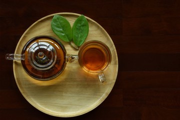 Top view  of teapot and tea cup with green near put the wooden plate on brown wood floor, copy space for text