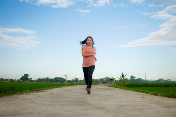 Wall Mural - outdoors jogging workout - young happy and dedicated Asian Chinese woman running at beautiful ccountryside road under a blue sky on enjoying fitness and cardio activity