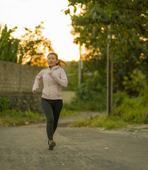 Wall Mural - outdoors running workout - young happy and dedicated Asian Chinese woman jogging at beautiful city park or countryside trail on sunset enjoying fitness and cardio activity