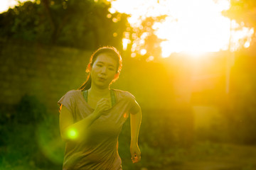 Wall Mural - outdoors running workout - young happy and dedicated Asian Korean woman jogging at beautiful city park or countryside trail on sunset enjoying fitness and cardio activity