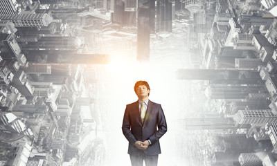 Young joyful businessman standing against city buildings background. Mixed media