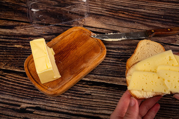 Someone is holding a fresh wheat toast with butter and cheese and a piece of butter in a wooden butter dish on a wooden background. Close up.