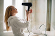 © JustLife - Beautiful women enjoying in hotel room. Young happy smiling woman wearing bathrobe using hair dryer in bathroom.