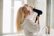 © JustLife - Beautiful women enjoying in hotel room. Young happy smiling woman wearing bathrobe using hair dryer in bathroom.