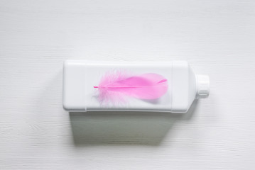 Wall Mural - White detergent bottle and pink bird feather on white wooden table flat lay background.