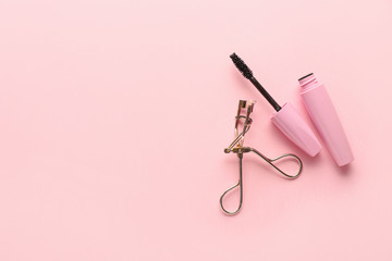 Mascara and eyelash curler on color background