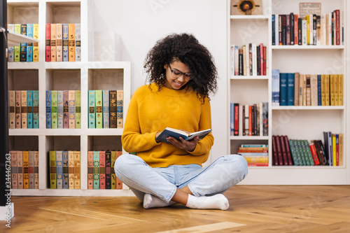 Fotomural Image of joyful african american woman reading book while sitting