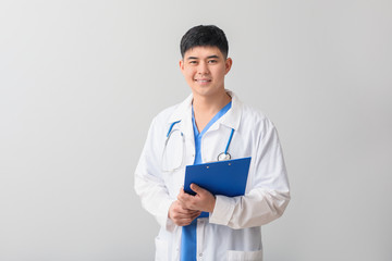 Wall Mural - Male Asian doctor with clipboard on light background