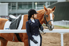 Beautiful Professional Female Jockey Standing Near Horse. Woman Horse Rider Is Preparing To Equitation. Girl And Horse. Equestrian Sport Concept. Dressage Horse 