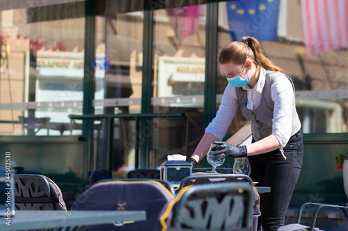 Waitress with a mask disinfects the table of an outdoor bar, café or restaurant, reopen after quarantine restrictions