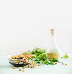 Healthy salad making ingredients on white table at light sunny wall background. Fresh kitchen herbs. Nuts topping. Olives oil. Salad dressing . Diet or vegetarian food concept.