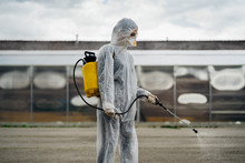 Sanitation Worker In Hazmat Protection Suit And N95 Mask With Chemical Decontamination Sprayer Tank.Disinfecting Streets And Public Areas To Stop COVID-19 Spread.Coronavirus Disinfection Concept