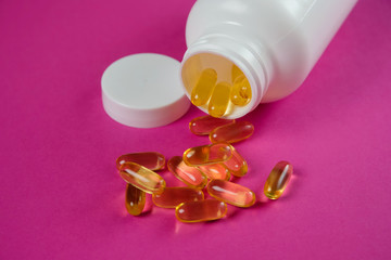 Yellow omega 3 fish oil capsules spilling out of white bottle on a purple background.