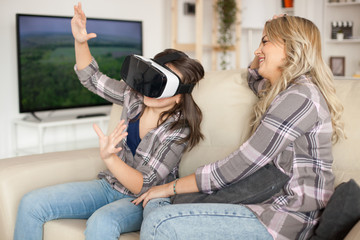 Wall Mural - Beautiful mother laughing while her daughter is playing games using virtual reality headset.