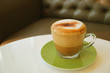 Cup of hot cappuccino coffee served on white round table with blurry sofa in background	