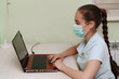 © svetograph - A young beautiful woman in a mask uses a laptop while sitting at her workplace. Technology, business, homework, online learning, concept of learning, communication with loved ones quarantine distance