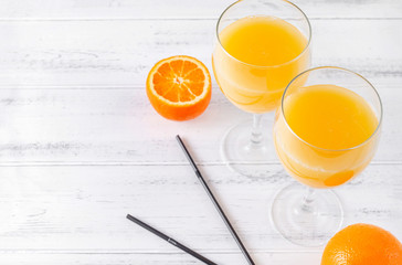 glasses of fresh orange juice, half a ripe orange, 2 black tubes on a white wooden background