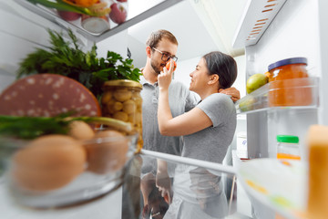 Look in the fridge. Young and successful couple in love looks in the fridge and take out of the fridge a bottle of milk while standing in the kitchen and makes breakfast.