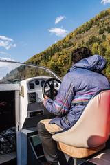 Wall Mural - Skipper at the helm of a motor boat, view from the cockpit. Fall. Russia, Altai Republic, Lake Teletskoye