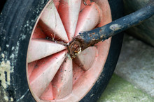 Close Up Of A Plastic Wheel Connected To An Old Rusty Metal Wheelbarrow.  Showing Colour Fade Due To Years Of Being Out In The Sun.