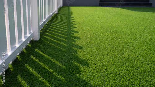 Fotomural Sunlight and shadow of white wooden fence on green artificial turf surface in fr
