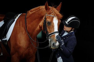 Portrait of a red dressage horse and young woman on black background. Girl with horse. Equestrian sport