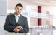 © nyul - Serious, young caucasian businessman checking time at business center. Standing, looking at camera, suit and tie, suitcase, copyspace.