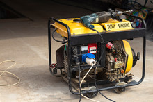 Stand-alone Diesel Generator To Supply Electricity In An Emergency. Yellow Color. Serves Not A Large Residential Building. On It Lies An Electric Drill
