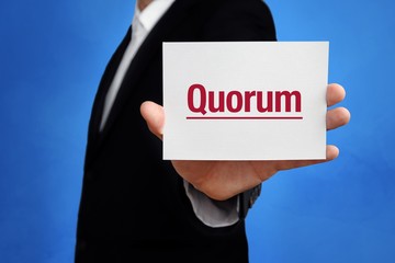 Wall Mural - Quorum. Lawyer in a suit holds card at the camera. The term Quorum is in the sign. Concept for law, justice, judgement