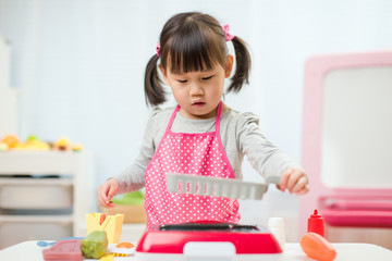 toddler girl pretend play food preparing role at home agianst white background