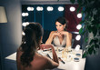 Beautiful woman applying make up for a evening date in front of a mirror. Focus on her reflection