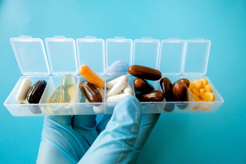 Wall Mural - A hand with a medical glove holds multi-colored capsules, a pill box with medicines on a blue background.