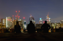 Rear View Of Friends Sitting Against 30 St Mary Axe In City At Night