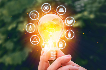 Wall Mural - hand holding light bulb against nature on green leaf with icons energy