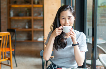 Young beautiful girl holding a cup of coffee in cafe. Outdoor portrait of young beautiful woman posing while traveling holiday vocation. Girl with coffee. Female traveler, Asian women drinking coffee.