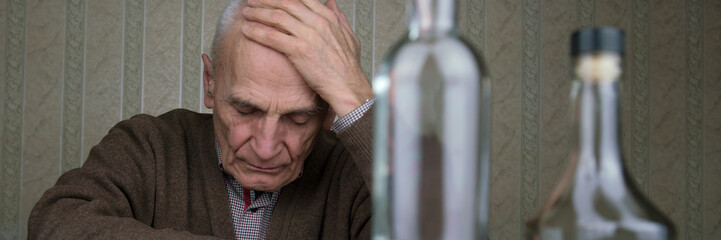 depressed alcoholic holds hand on head sitting at table with bottles of vodka and cognac